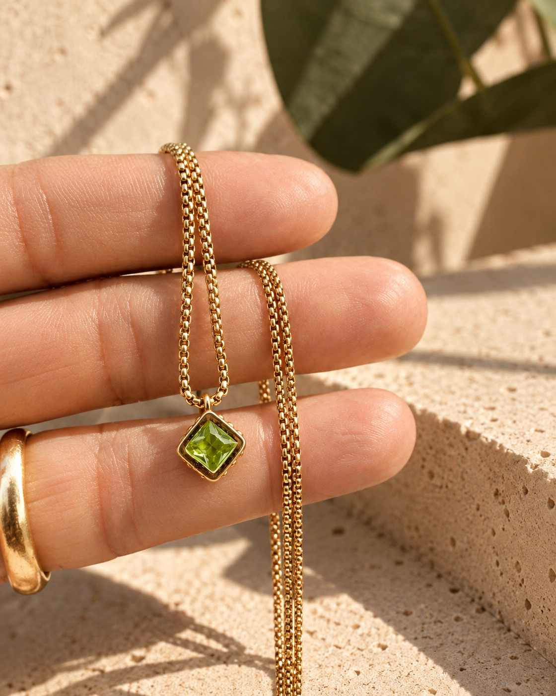 Pendentif cube péridot TESEO plaqué or 18 carats tenu en main, sur travertin